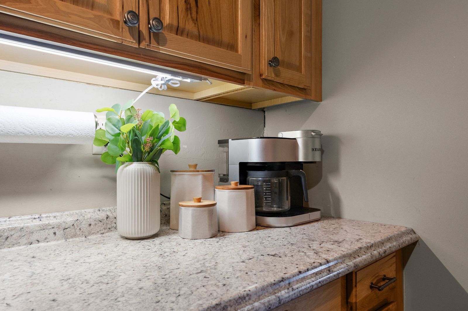 Coffee maker and ceramic canisters on a granite counter under warm cabinet lighting