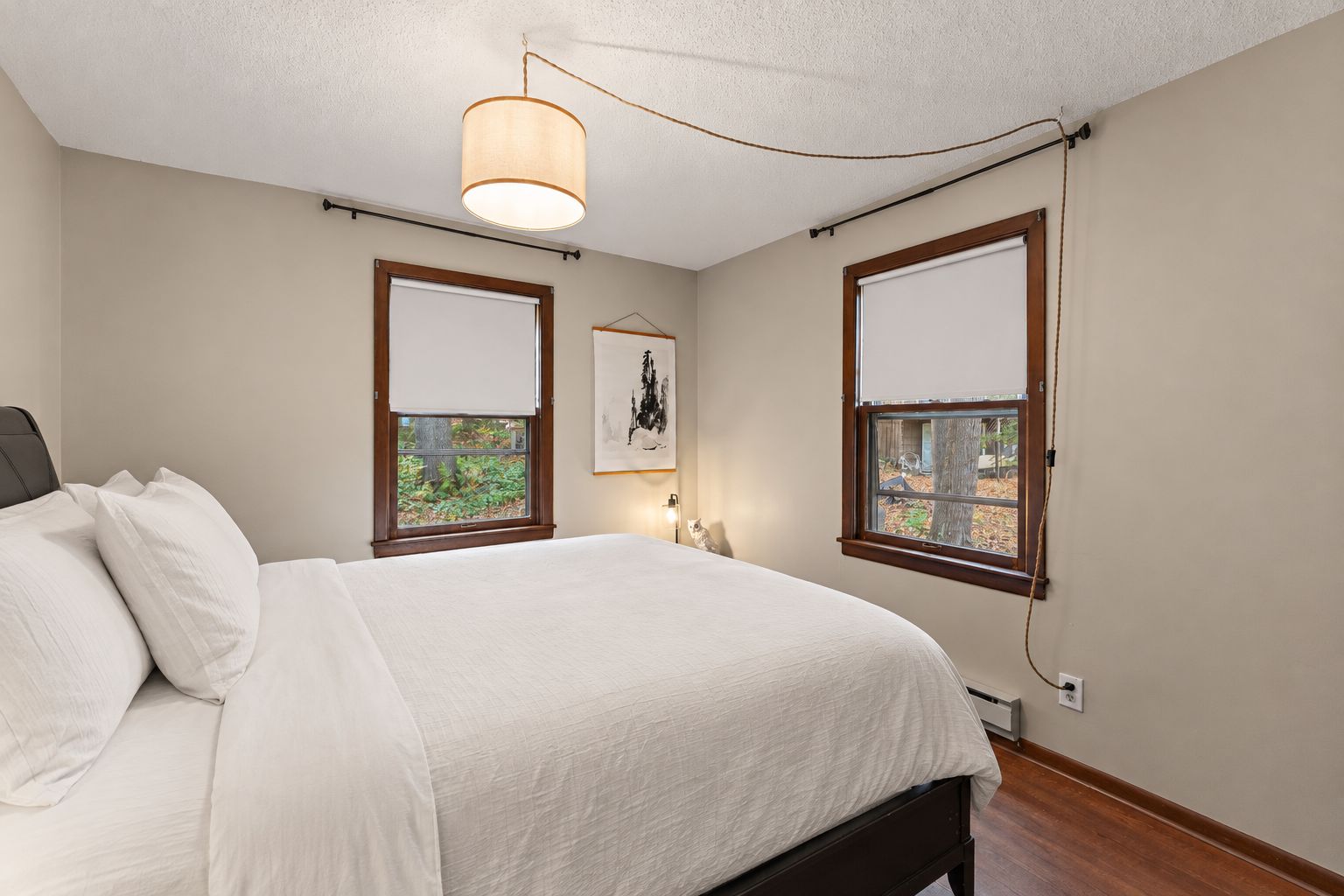 Bedroom with a bed in crisp white linens, a woven pendant lamp, and two wood-framed windows